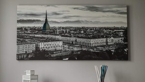 A black and white cityscape with a prominent tower, a row of buildings, and a small white object on a table.