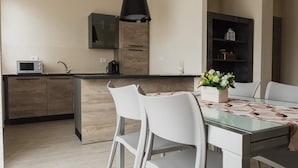 A modern kitchen with a microwave, sink, and a black range hood. There is a dining area with a glass table and white chairs.