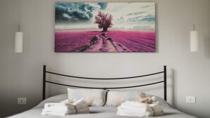 A bedroom with a bed, pillows, and a wall-mounted painting of a tree in a field.