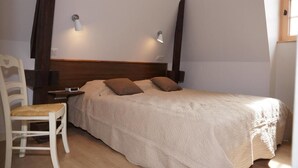 Une chambre à coucher comprenant un lit, deux lampes fixées au mur, une tête de lit en bois, une table de chevet et une chaise.