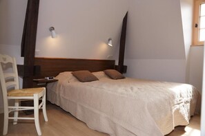 A bedroom with a bed, two wall-mounted lights, a wooden headboard, a bedside table, and a chair.