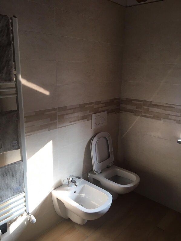 A small bathroom with two toilets, a bidet, and a towel rack.