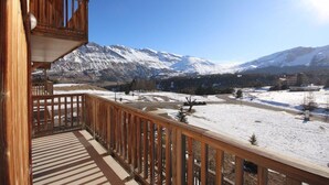 A wooden balcony with a view of snow-covered mountains and a clear sky.