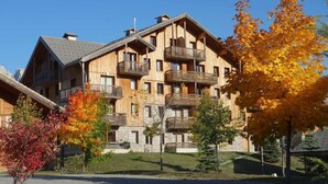 A multi-story wooden building with balconies, surrounded by autumn foliage.