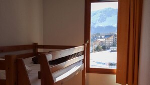 A small, narrow room with a bunk bed, a window with a view of a snowy landscape, and a radiator.