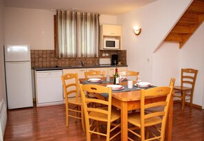 A dining area with a wooden table and chairs, a kitchen with a microwave, and a staircase. - Chalet, 300m from ski slopes, swimming pool, sauna, terrace, parking, tv, ski locker, 56m² (Le Dévoluy)