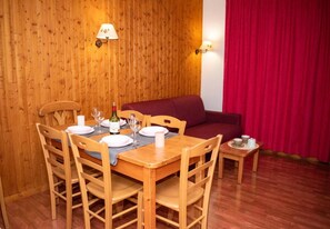 Uma mesa de jantar de madeira com cadeiras, um sofá vermelho e uma pequena mesa lateral com chávenas e uma garrafa.