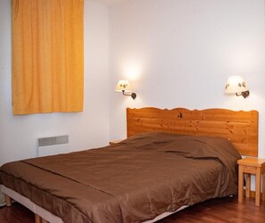 Uma cama bem arrumada com colcha marrom, duas luminárias na parede e uma mesa de cabeceira de madeira.