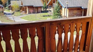 Eine Holzterrasse mit dekorativer Geländer, die auf einen Wohnbereich mit Häusern und einem bewaldeten Hügel blickt.