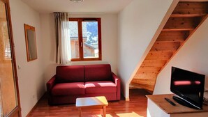 Ein gemütlicher, kompakter Wohnraum mit einem roten Sofa, einem kleinen Tisch, einem Fernseher und einer Holztreppe.