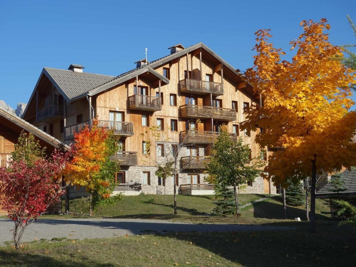 A multi-story wooden building with balconies, surrounded by autumn foliage.
