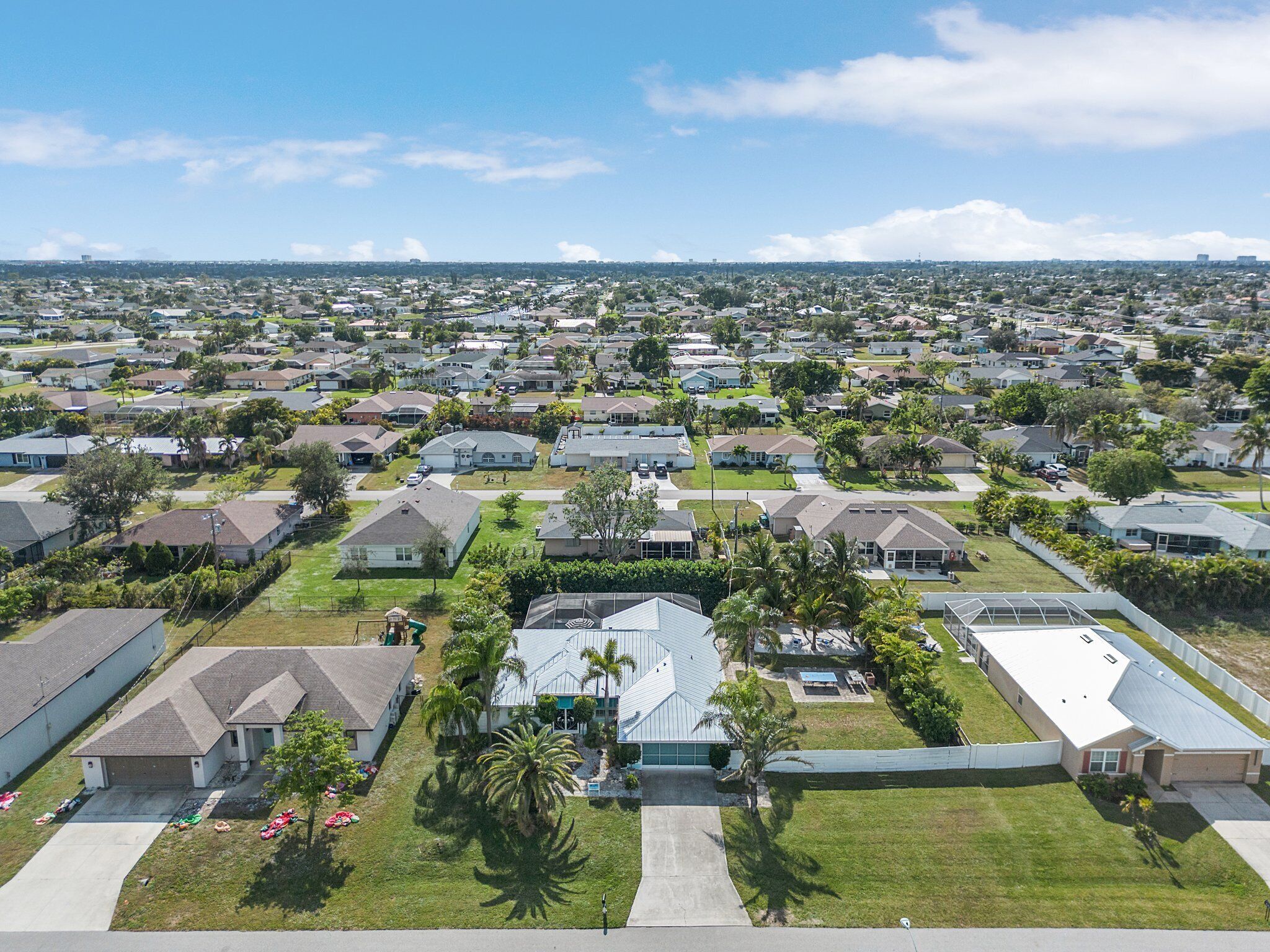 A residential area with houses, green lawns, and palm trees.
