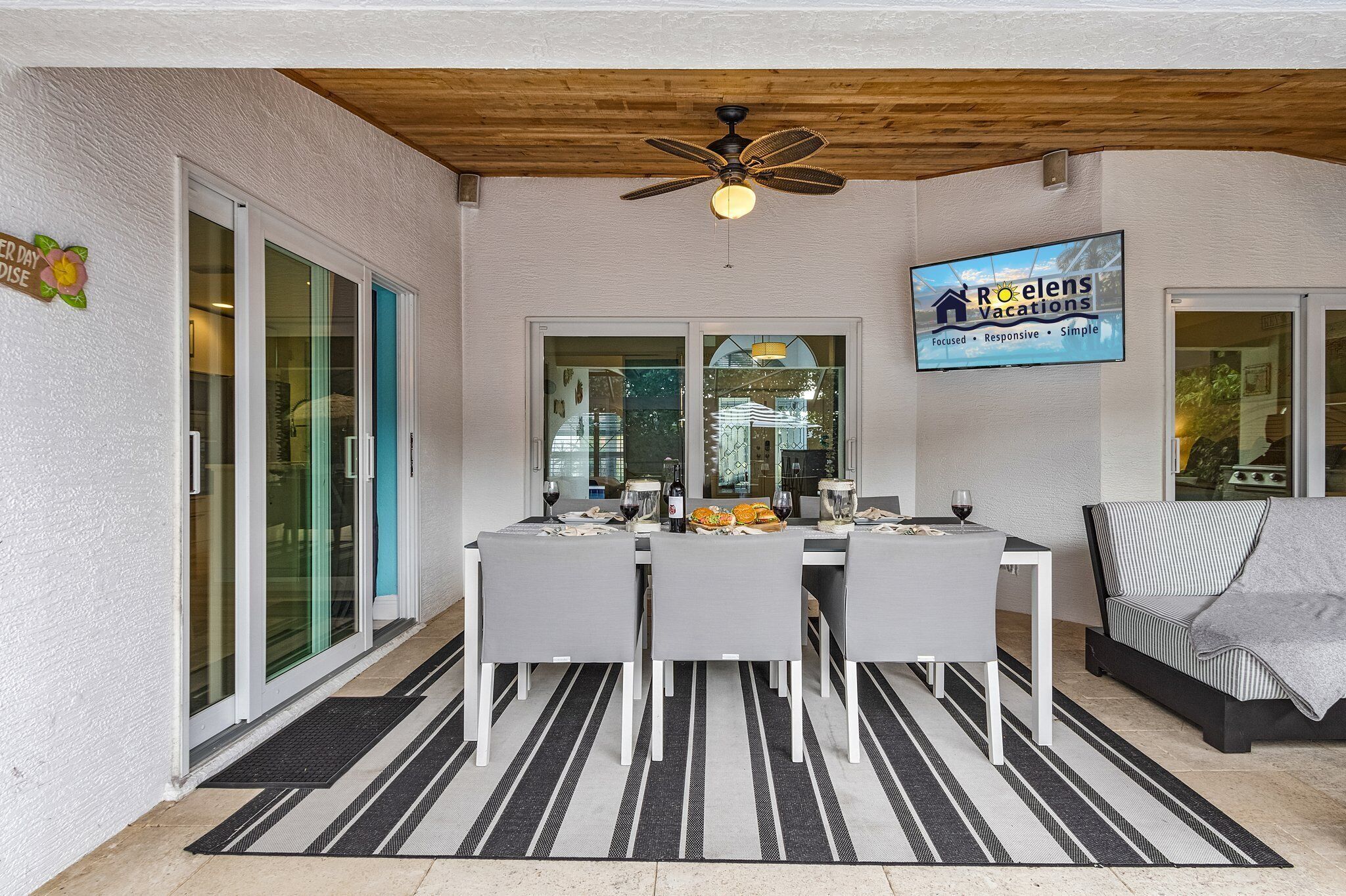 Comedor con una mesa dispuesta para cuatro, un ventilador de techo y un cartel de Roelens Vacations.