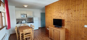 Cocina compacta con microondas, tostadora y cafetera, una mesa de comedor con sillas y un televisor sobre un mueble de madera.