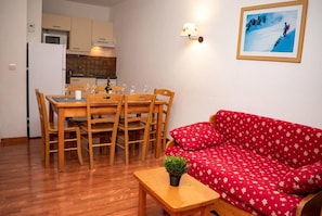 A compact living space with a dining area, a red sofa, and a small table with a plant. - 300m from shops, 2nd floor, view mountain/resort, swimming pool, sauna, balcony, parking, tv (Le Dévoluy)