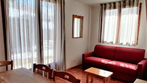 A living room with a red sofa, wooden dining table, and chairs. - Chalet, 300m from ski slopes, swimming pool, sauna, terrace, parking, tv, ski locker, 42m² (Le Dévoluy)