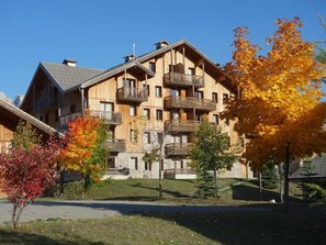 A multi-story wooden building with balconies, surrounded by autumn-colored trees. - Chalet, 300m from shops, swimming pool, sauna, terrace, parking, tv, ski locker, 45m², Superdévoluy (Le Dévoluy)