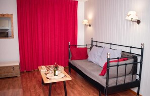 A cozy room with a bed, a small table with a bottle and glasses, a red curtain, and two wall-mounted lamps. - 300m from ski slopes, 3rd floor, swimming pool, sauna, balcony, parking, tv, ski locker, 45m² (Le Dévoluy)