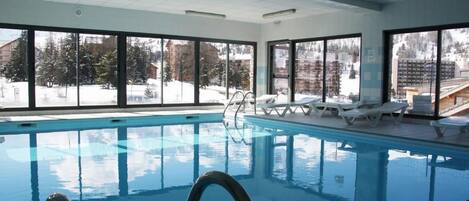 An indoor swimming pool with clear views of a snowy landscape through large windows.