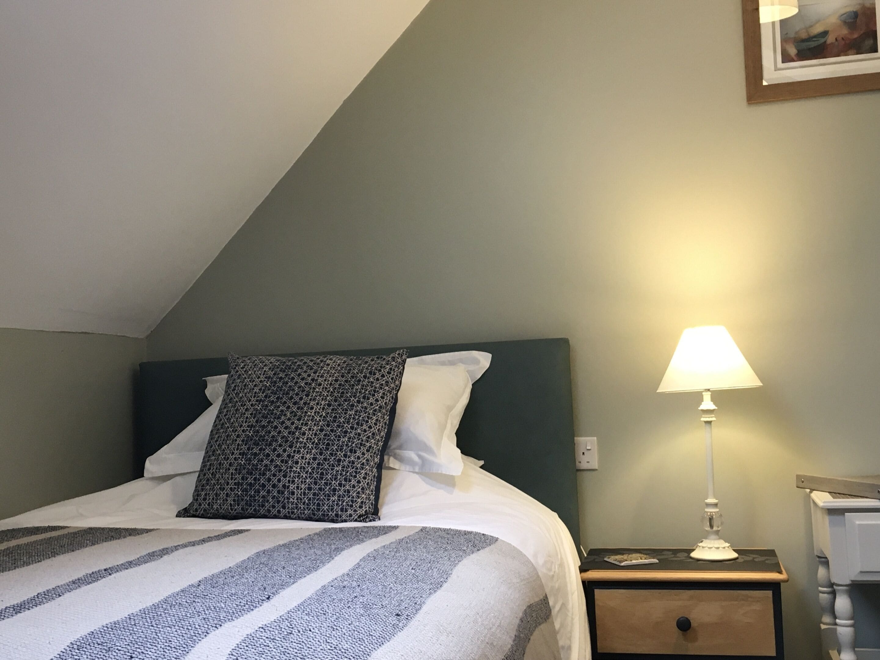 Una cama bien hecha con ropa de cama a rayas, una almohada estampada y una lámpara de noche sobre una mesita de madera.