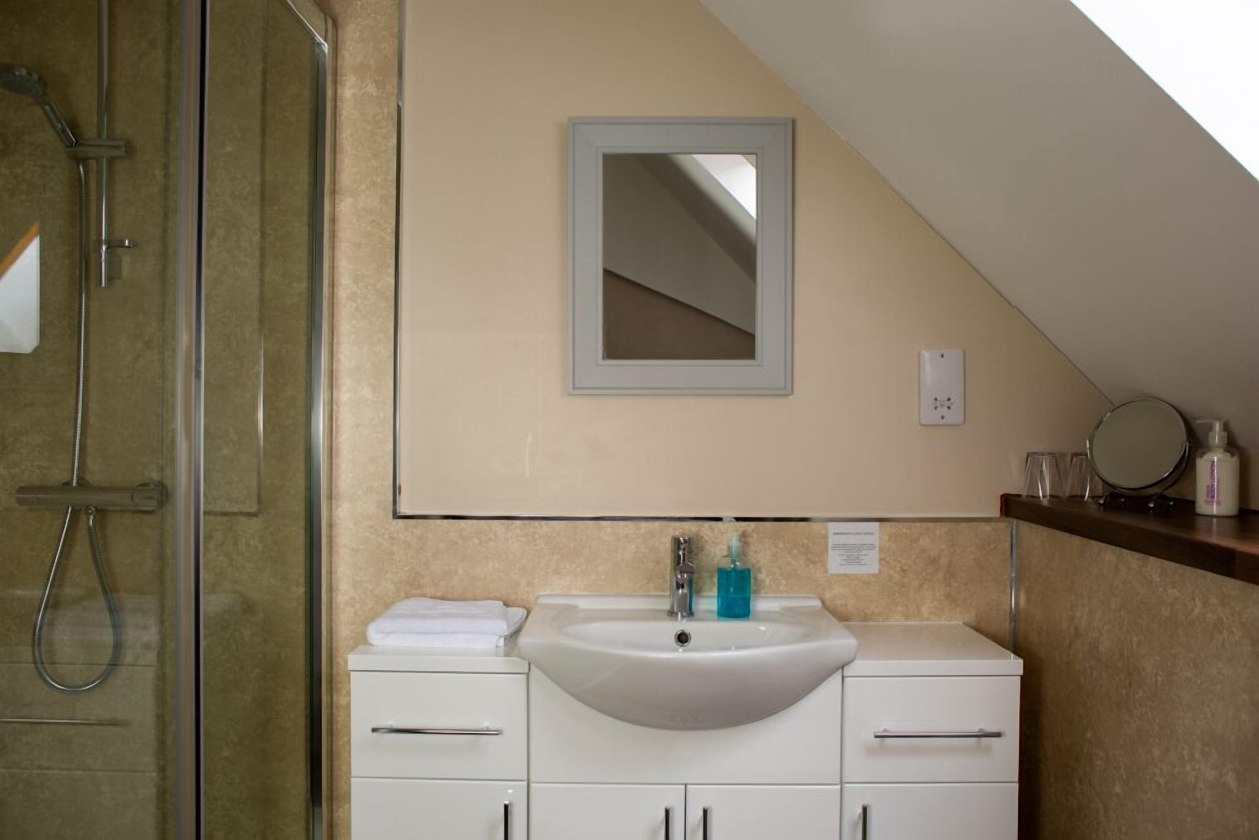 Un bagno con box doccia in vetro, lavandino bianco con specchio sopra e parete rivestita in piastrelle color beige.