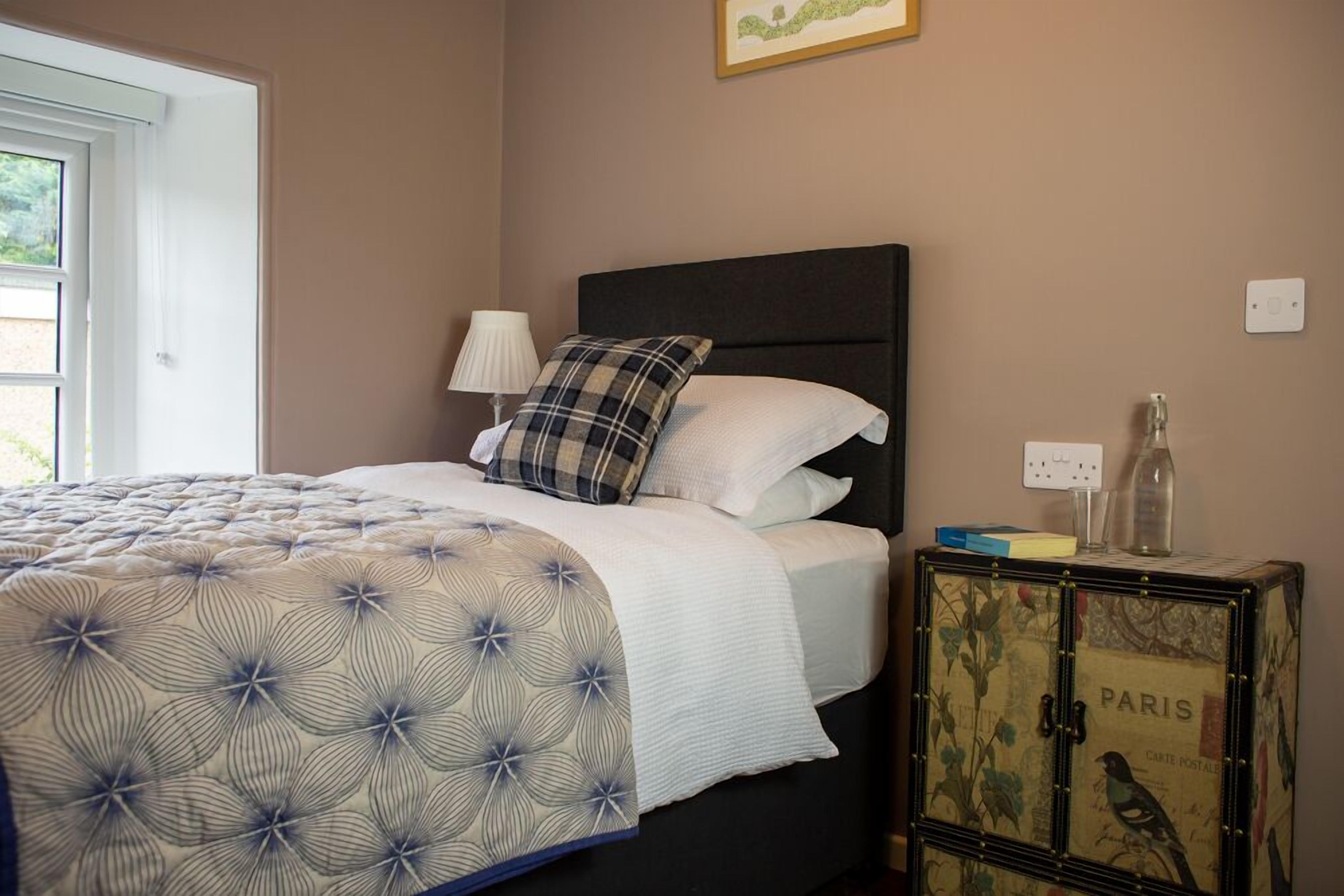 A bedroom with a bed, a nightstand, a lamp, a cabinet with a vintage design, and a window.