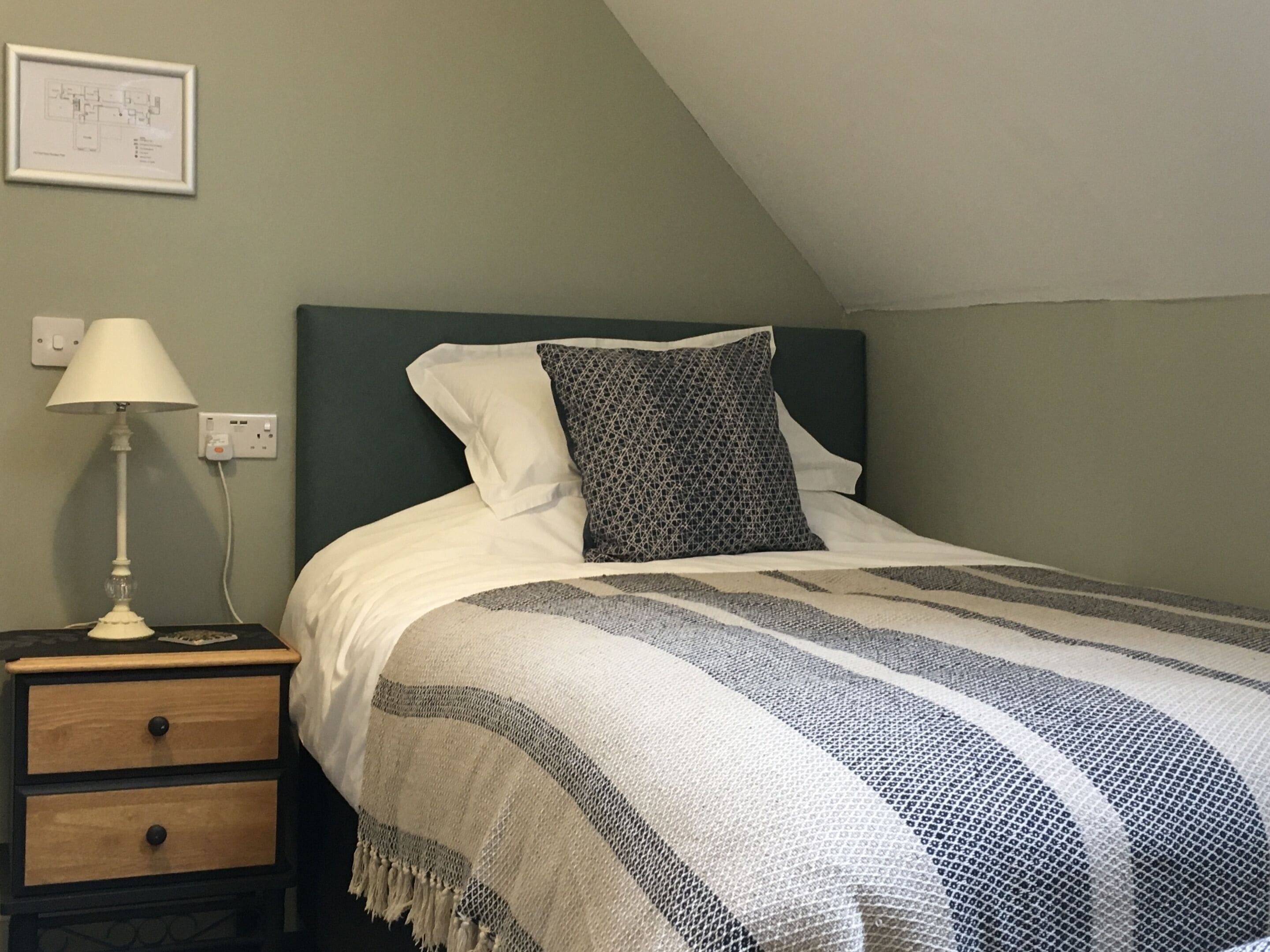 A bedroom with a bed, a nightstand, a lamp, and a wall-mounted light switch.