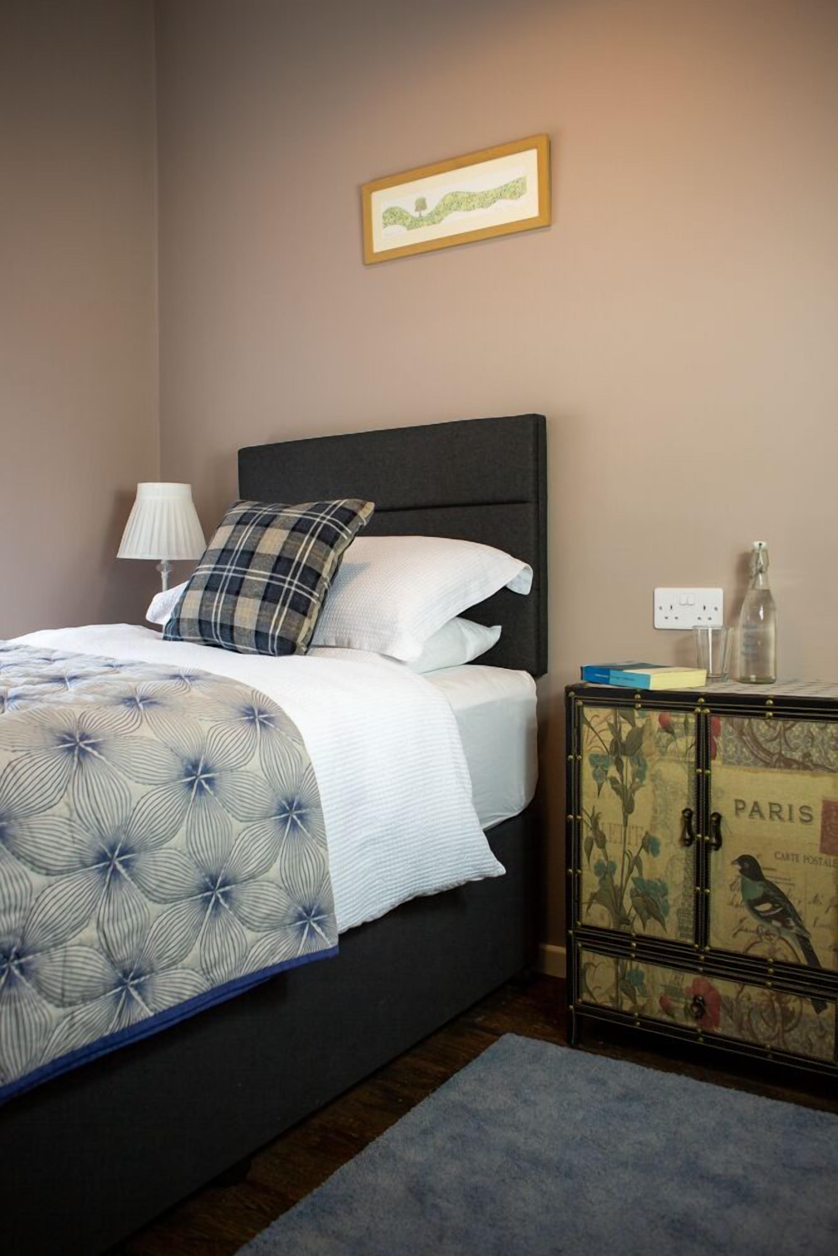 A neatly made bed with a patterned bedspread, a dark headboard, and a small bedside table with a lamp and a decorative item.