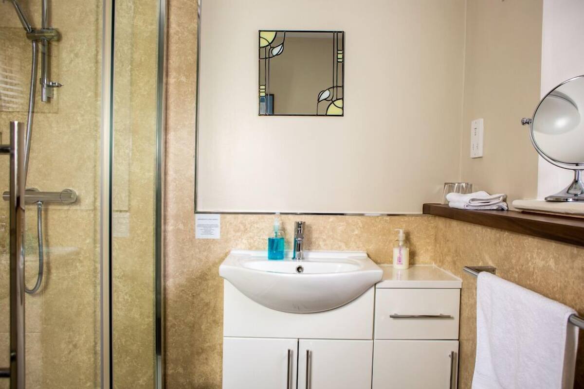 A bathroom with a glass shower enclosure, a white sink with a mirror above it, and a towel rack.