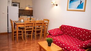 A compact living space with a dining area, a red sofa, and a small table with a plant. - 300m from ski slopes, Ground floor, view resort, swimming pool, sauna, balcony, parking, tv (Le Dévoluy)