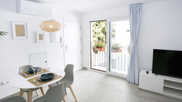 A modern living room with a dining area, a TV, and a sliding glass door to a balcony with plants.