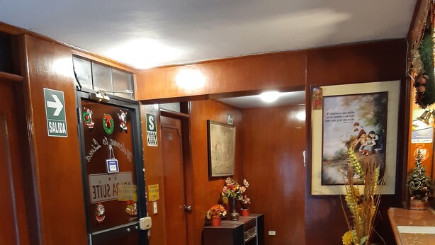 A hotel reception area with a wooden interior, a reception desk, a framed picture, and a decorative vase with flowers. - Aruba Suite Hotel (Lima)