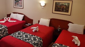 A hotel room with two beds, each with a red bedspread and white pillows. There are framed pictures on the walls, a bedside table with a lamp, and a small potted plant on the nightstand. - Aruba Suite Hotel (Lima)
