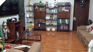 A living room with a TV, sofas, a coffee table, and a bookshelf filled with books and Christmas decorations. - Aruba Suite Hotel (Lima)