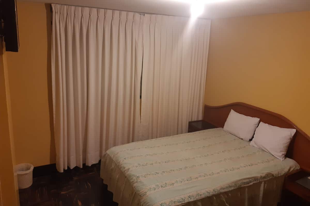 A hotel room with a bed, a nightstand, a lamp, and a curtain.