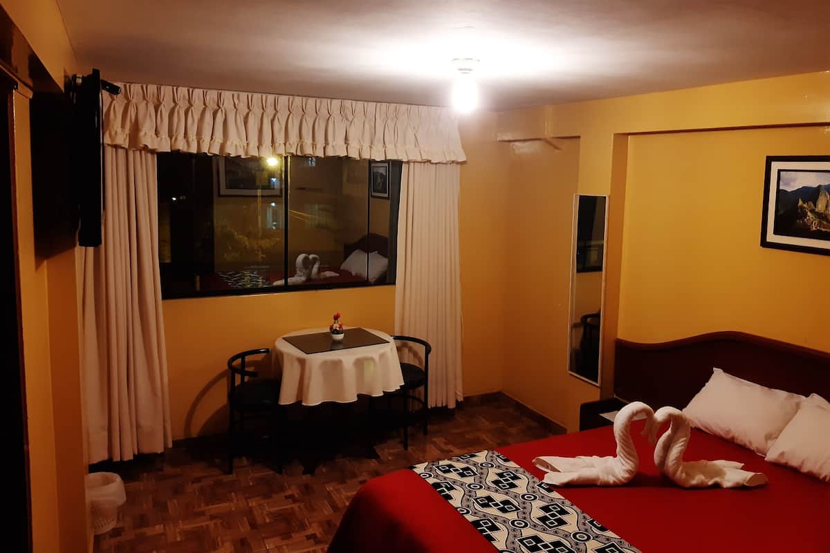 A hotel room with a bed, a table with chairs, a window with curtains, and a painting on the wall.