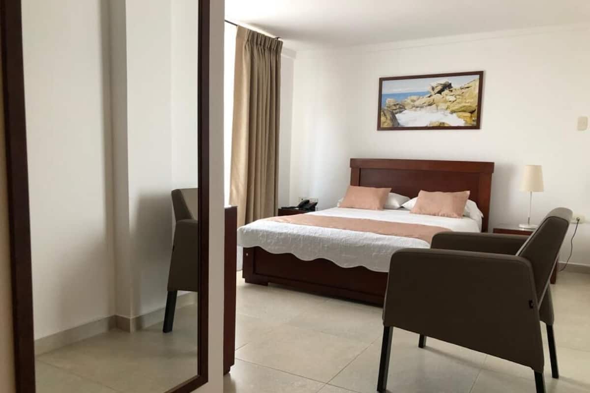 A hotel room with a bed, a chair, a nightstand, and a painting on the wall.