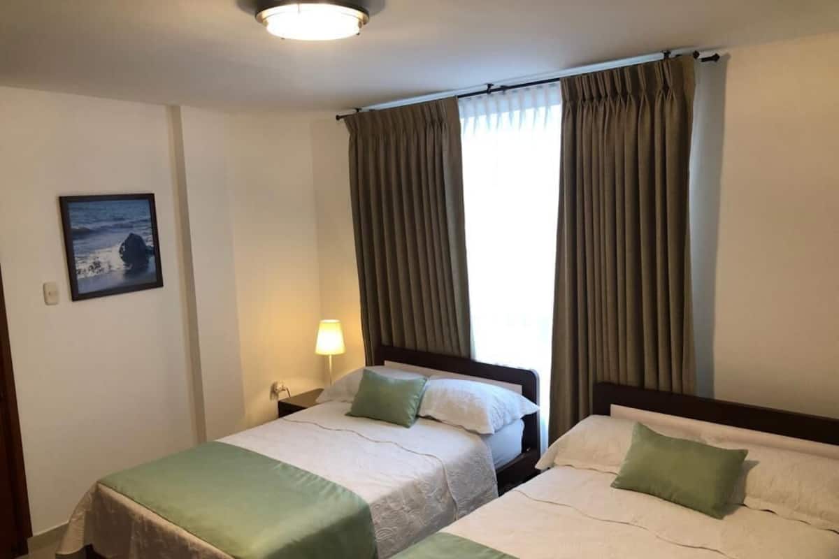 A hotel room with two beds, a nightstand, a lamp, and a framed picture on the wall.