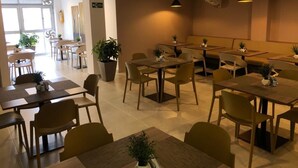 A modern dining area with multiple tables and chairs, potted plants, and pendant lighting. - Colón Plaza Hotel (Tumaco)