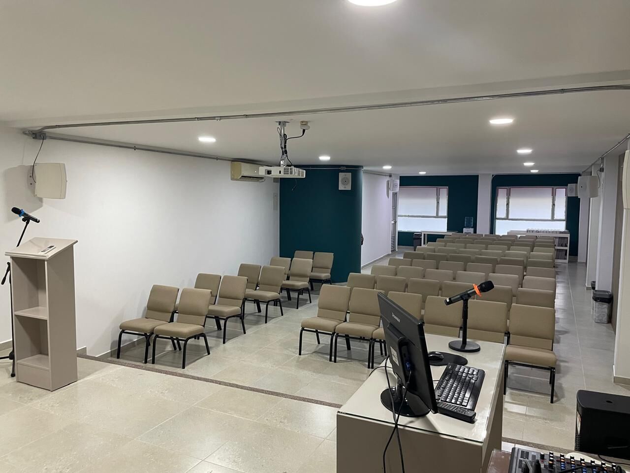 Un salón de conferencias con filas de sillas, un atril, un proyector y un equipo de ordenador.