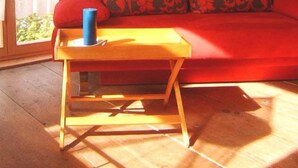 A cozy living room with a red sofa, patterned cushions, a wooden coffee table, and a wooden cabinet.