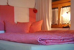 A bed with red and white checkered bedding, a heart-shaped decoration, and a window with lace curtains. - BioPension Kirschenfee (Sontheim)