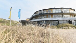 A modern, multi-story building with a curved roof, situated on a grassy hill. - De Duynsuites (Callantsoog)
