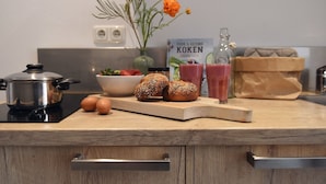 A kitchen counter with a pot, eggs, bread, a bowl of fruit, and a vase with flowers. - De Duynsuites (Callantsoog)