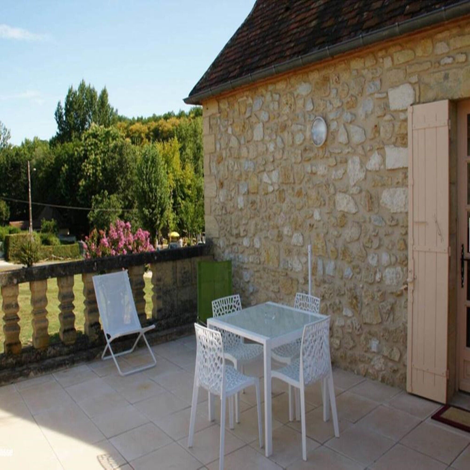 Un bâtiment en pierre doté d’une terrasse carrelée, d’une table avec des chaises et d’une porte.