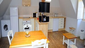 Una cocina compacta con una mesa y sillas de madera, lavadora, microondas y televisor.