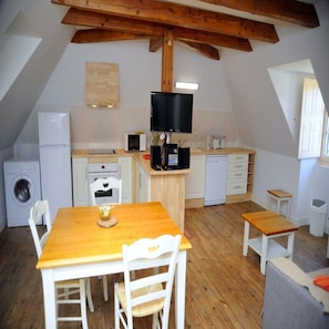 A compact kitchen with a wooden table and chairs, a washing machine, a microwave, and a television.