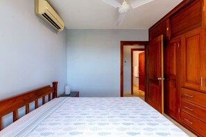 Un dormitorio con cama, armario de madera, ventilador de techo y aire acondicionado.