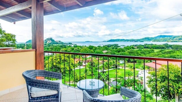 A balcony with wicker furniture and a view of a lush landscape. - Coastal-Inspired Condo w/ Infinity Pool & Oceanview Terrace (Playa Flamingo)