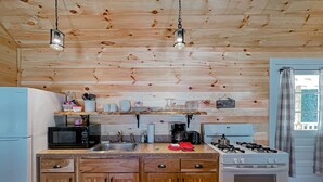 A kitchen with wooden cabinets, a stove, a sink, and a microwave. - Mrs. Otis's Cabin with Woodland View (Paul Smiths)